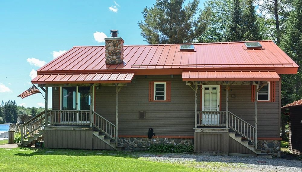 House with a red standing seam metal roof, a stone chimney and covered porch