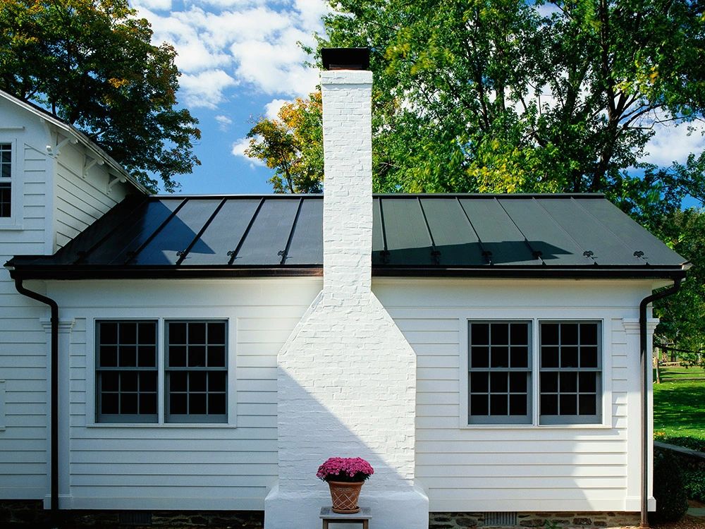 White home with a dark green metal roof and brick chimney